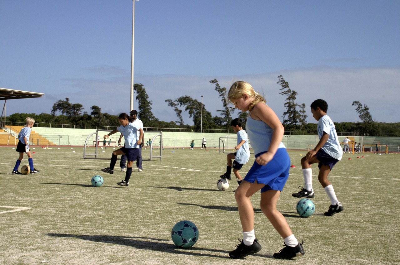 Kids learning how to play soccer by dribbling the ball on an outdoor pitch.